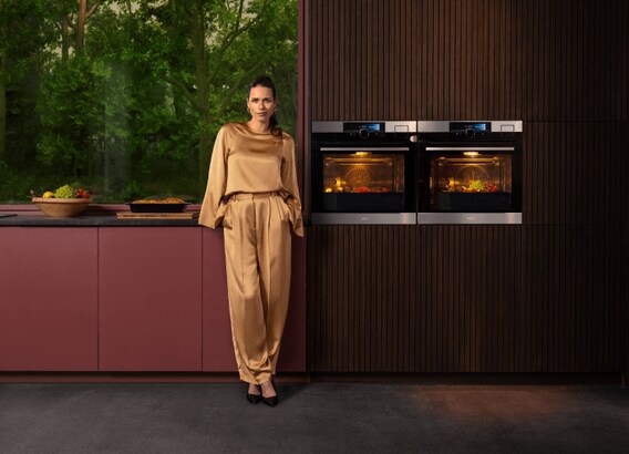 Woman standing next to two ovens in a kitchen.